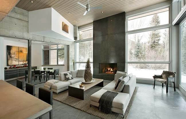 中立的な色とコンクリートのグレースケールの特性を持つこの美しい家は、雪で覆われた松の木の中にあります。寒さとシンプルな外見とは対照的に、インテリアは非常に居心地が良く、自然光で満たされています。あなたは暖かい歓迎の家として近代的な暖炉とキッチンとリビングルームのオープンスペースを参照してください内に入る